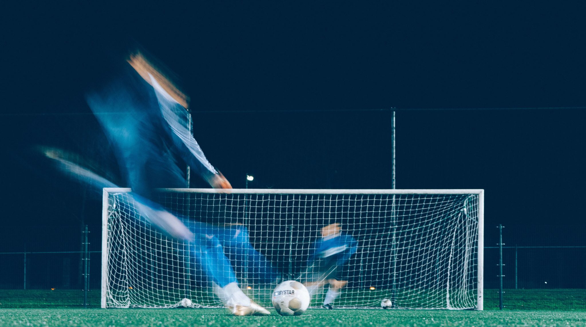 Artistic shot of footballer kicking ball towards goal and goalkeeper